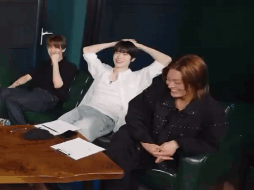 A Group Of People Are Sitting At A Table With Their Arms Over Their Head . GIF