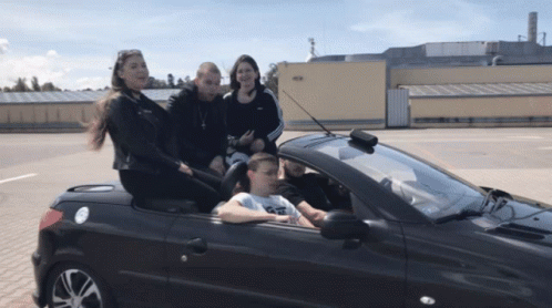 A Group Of People Are Sitting In A Convertible Car With A Man Driving GIF