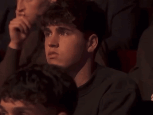 A Group Of People Are Sitting In A Dark Room And One Of Them Is Looking At Something GIF