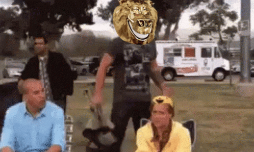 A Group Of People Are Sitting In A Park With A Lion 'S Head Above Them GIF