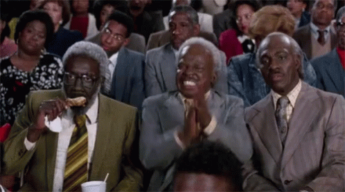 A Group Of People Are Sitting In A Room And One Man Is Eating A Piece Of Food GIF