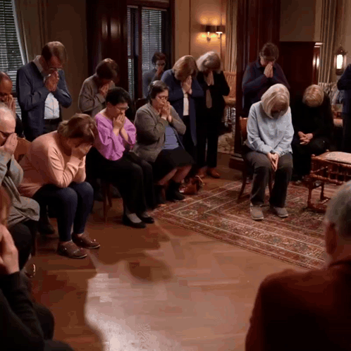 A Group Of People Are Sitting In A Room And Praying GIF