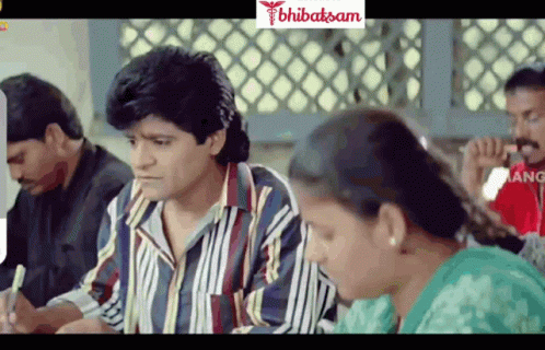 A Group Of People Are Sitting In A Room With A Sign That Says ' Bhibatasan ' GIF
