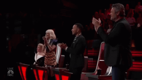 A Group Of People Are Sitting In A Stadium Applauding A Performance . GIF