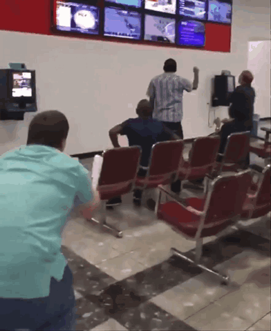 A Group Of People Are Sitting In A Waiting Room With A Tv On The Wall GIF
