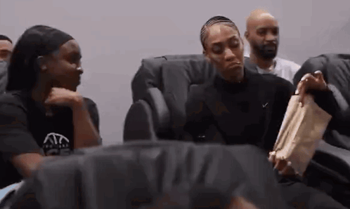 A Group Of People Are Sitting In Chairs Talking To Each Other . GIF
