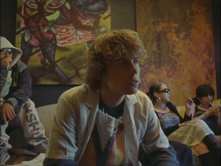 A Group Of People Are Sitting In Front Of A Painting And One Of Them Is Wearing A Jacket That Says Ash On The Bottom GIF