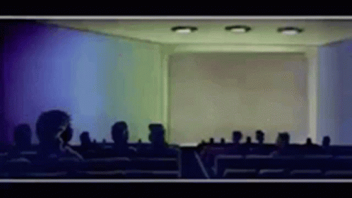 A Group Of People Are Sitting In Front Of A Screen In A Room GIF