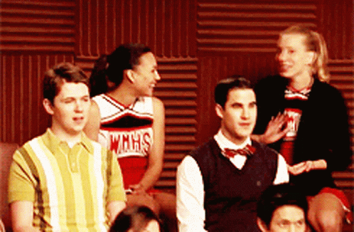 A Group Of People Are Sitting In Front Of A Wall And One Of The Cheerleaders Is Wearing A Wmhs Shirt GIF