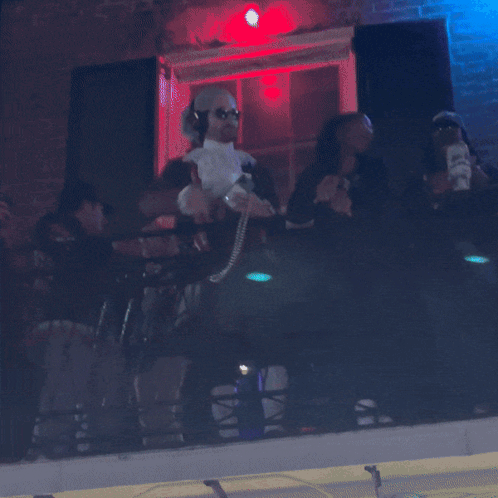 A Group Of People Are Sitting On A Balcony With A Purple Light Behind Them GIF