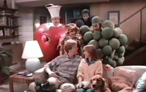 A Group Of People Are Sitting On A Couch In A Living Room With A Giant Apple Behind Them . GIF
