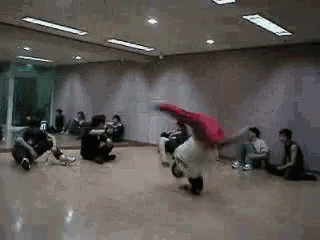 A Group Of People Are Sitting On The Floor In A Dance Studio Watching A Person Do A Trick . GIF