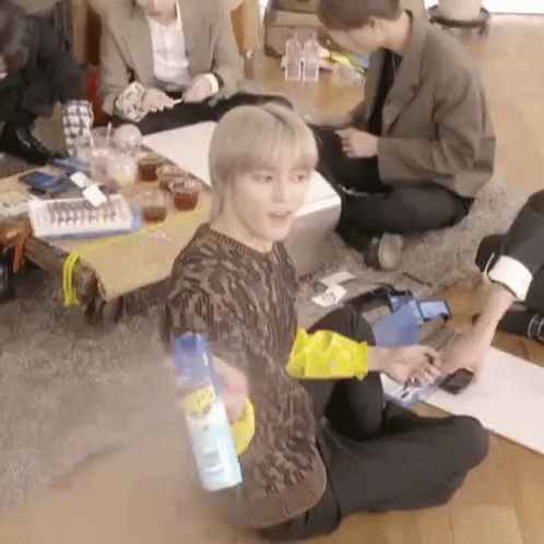A Group Of People Are Sitting On The Floor In A Living Room . One Of The Men Is Holding A Spray Bottle . GIF