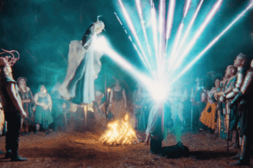 A Group Of People Are Standing Around A Fire With A Blue Light Coming Out Of The Sky GIF
