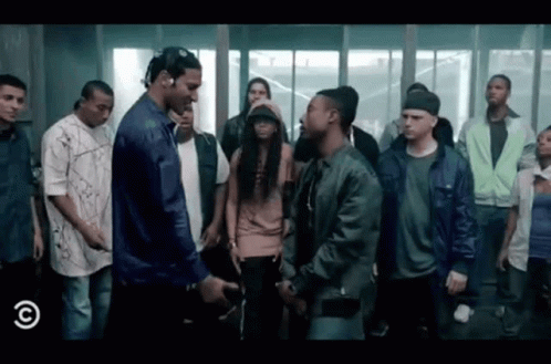 A Group Of People Are Standing Around A Man In A Blue Jacket . GIF
