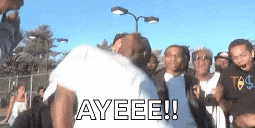 A Group Of People Are Standing Around A Man In A White Shirt With The Word Ayeeee Written On It . GIF