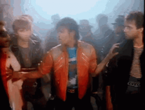 A Group Of People Are Standing Around A Man In An Orange Jacket . GIF