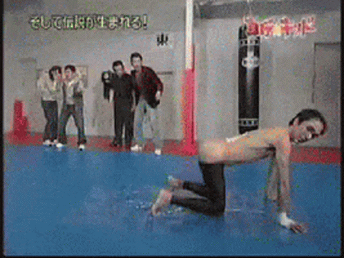 A Group Of People Are Standing Around A Man On His Knees In A Gym GIF