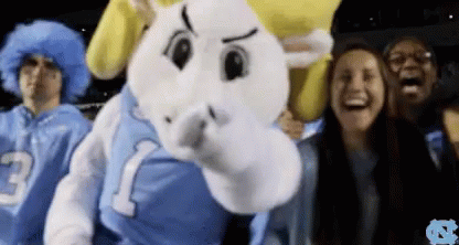 A Group Of People Are Standing Around A Mascot Wearing A Jersey With The Number 1 On It GIF
