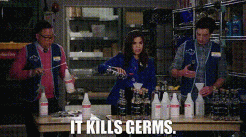 A Group Of People Are Standing Around A Table With Bottles Of Cleaning Supplies And The Words `` It Kills Germs '' . GIF