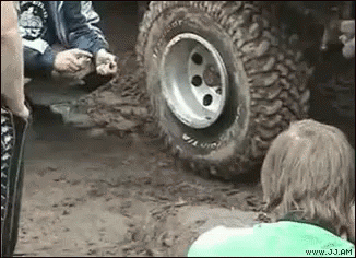 A Group Of People Are Standing Around A Tire Of A Jeep . GIF
