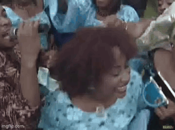 A Group Of People Are Standing Around A Woman In A Blue Dress Holding A Microphone . GIF