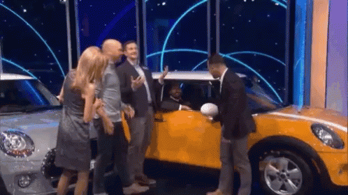 A Group Of People Are Standing Around A Yellow Mini Cooper . GIF