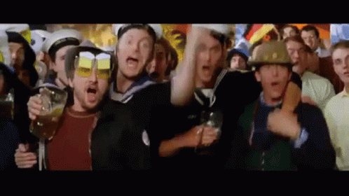 a group of people are standing in a crowd holding glasses of beer and wearing helmets .