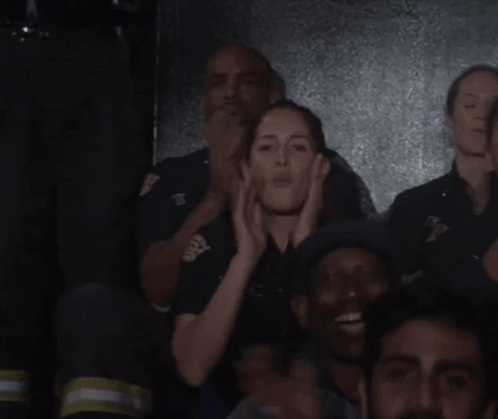 A Group Of People Are Standing In A Dark Room And One Of Them Is Wearing A Black Shirt With The Letter T On It GIF