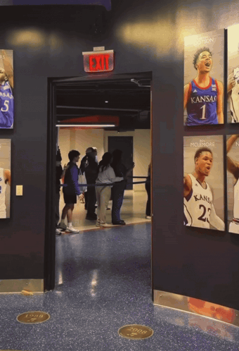 A Group Of People Are Standing In A Hallway With A Kansas Basketball Player On The Wall GIF