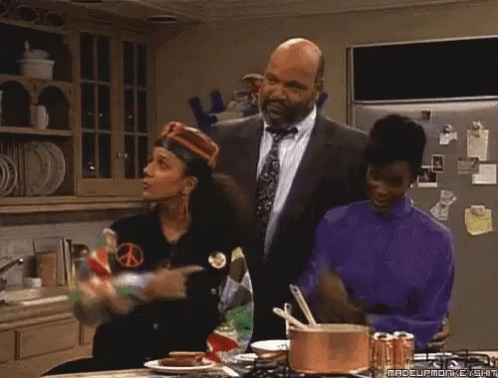 A Group Of People Are Standing In A Kitchen And One Of Them Has Her Fist Up GIF