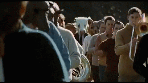 A Group Of People Are Standing In A Line Playing Musical Instruments . GIF