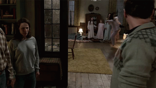 A Group Of People Are Standing In A Living Room With A Book Titled " The Conjuring " In The Background GIF