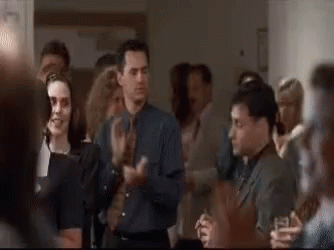 A Group Of People Are Standing In A Room Applauding Each Other . GIF
