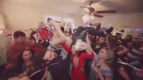 A Group Of People Are Standing In A Room With A Ceiling Fan . GIF