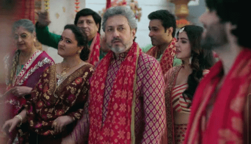 A Group Of People Are Standing In A Room With A Man Wearing A Red Scarf Around His Neck . GIF
