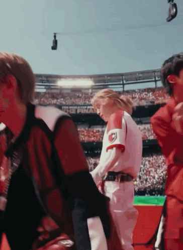 A Group Of People Are Standing In A Stadium And One Of Them Is Wearing A Red And White Jersey With The Letter R On It GIF