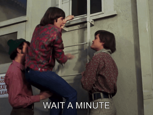 A Group Of People Are Standing In Front Of A Building With The Words Wait A Minute On The Bottom GIF