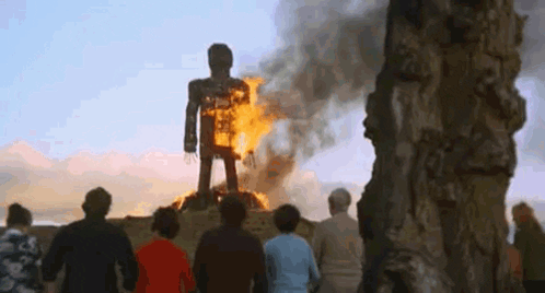 A Group Of People Are Standing In Front Of A Burning Statue Of A Man . GIF