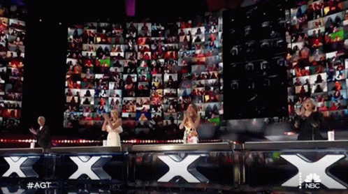 A Group Of People Are Standing In Front Of A Large Screen That Says Nbc GIF