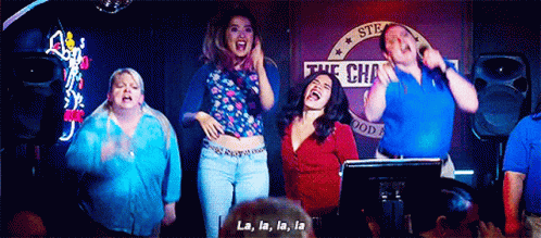 a group of people are standing in front of a microphone singing la la la la .
