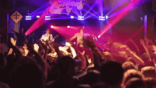 A Group Of People Are Standing In Front Of A Stage That Has The Word Tropicals On It GIF