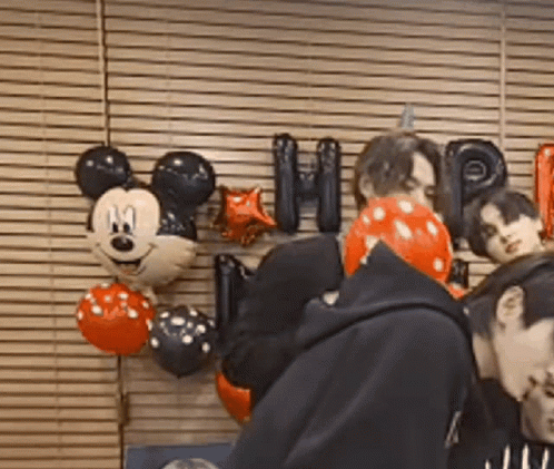 A Group Of People Are Standing In Front Of A Wall With Mickey Mouse Balloons And Letters . GIF