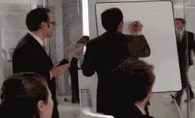 A Group Of People Are Standing In Front Of A White Board . GIF