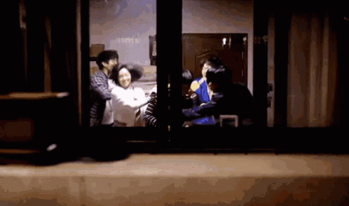 A Group Of People Are Standing In Front Of A Window And Talking To Each Other . GIF