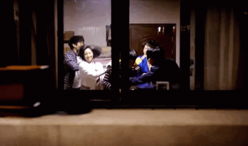 A Group Of People Are Standing In Front Of A Window In A Dark Room . GIF