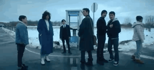 A Group Of People Are Standing Next To Each Other On The Side Of The Road In Front Of A Pay Phone Booth . GIF