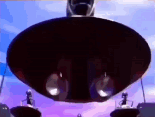 A Group Of People Are Standing On A Platform In Front Of A Large Black Object . GIF