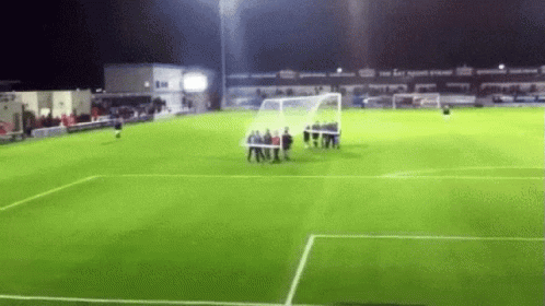 A Group Of People Are Standing On A Soccer Field At Night . GIF