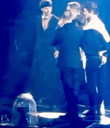 A Group Of People Are Standing On A Stage In Front Of A Microphone . GIF